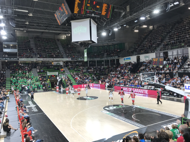 Basketballspiel in einer großen Halle mit Zuschauern, mit einem Spiel zwischen Asvel und Galatasaray, wie auf den Courtside-Boards zu sehen.