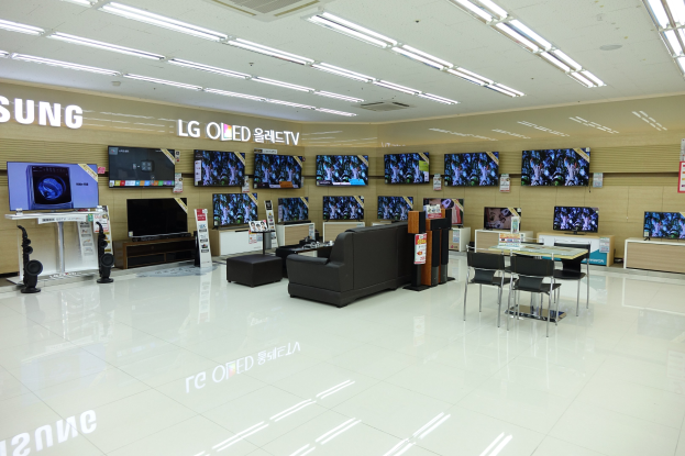 Ein geräumiger Raum mit mehreren an den Wänden montierten Fernsehern, umgeben von Sofas, Tischen, Stühlen und anderen Möbelstücken, beleuchtet von Deckenlampen.