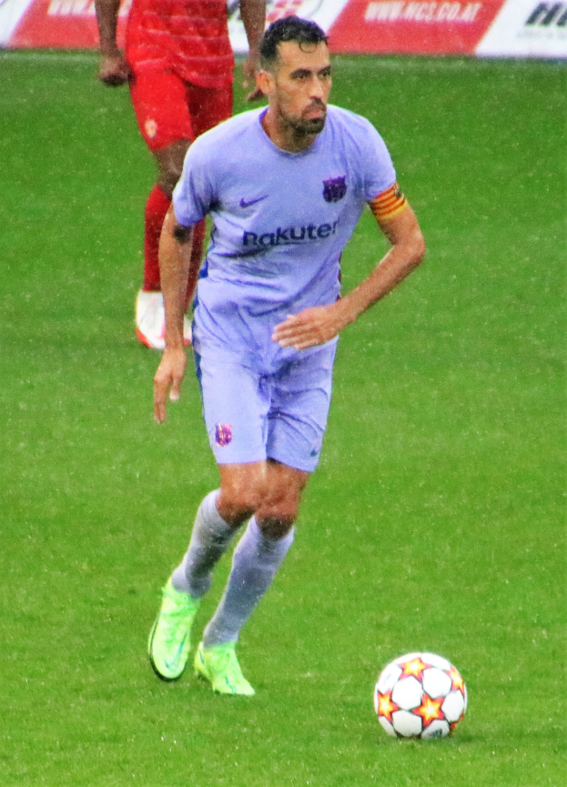 Ein Fußballer in Sportbekleidung und -schuhen ist im Einsatz auf dem Feld mit einer Texttafel im Hintergrund.