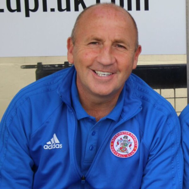 Zwei strahlende Männer in einem Raum, einer in einem blauen Jackett, wahrscheinlich der Trainer des Accrington Stanley Football Club, mit einer Tafel an der Wand dahinter.