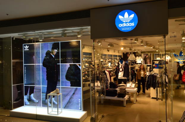 Ein Geschäft einer Adidas Originals-Filiale in einem Einkaufszentrum mit Schaufensterpuppen, hängender Kleidung, präsentierten Schuhen und beleuchteter Markenwerbung.
