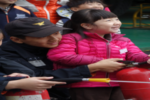 Gruppe von Kindern um einen roten Hydranten in einer Schulumgebung versammelt, ein Kind hält ein Rohr.