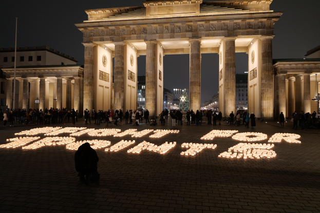 Eine Gruppe von Menschen steht vor dem beleuchteten Brandenburger Tor in Berlin, Deutschland, umgeben von Gebäuden, Pfählen und Lichtern; die Wörter 'Kampf für Freiheit' sind im Vordergrund sichtbar.