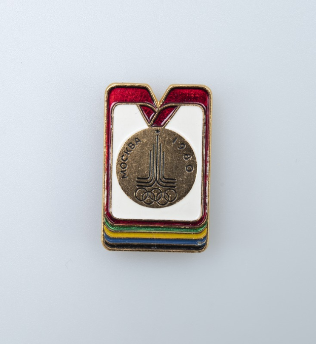 Eine weiße Fläche mit einem Abzeichen der Olympischen Winterspiele 1980 in Moskau, Russland, das ein farbenfrohes Design und die Inschrift 'Olympische Spiele' zeigt.