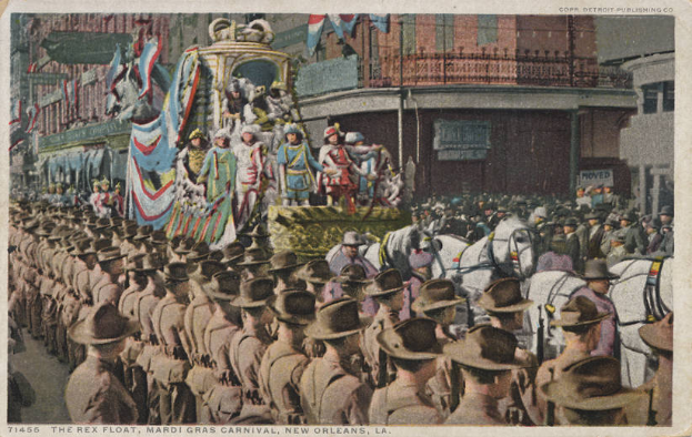 Eine alte Postkarte, die einen Mardi Gras-Umzug in New Orleans zeigt, mit Menschen zu Pferd, einem dekorierten Float mit Flaggen und Gebäuden im Hintergrund, und der Inschrift "The Rex Float, Mardi Gras Carnival, New Orleans" unten.