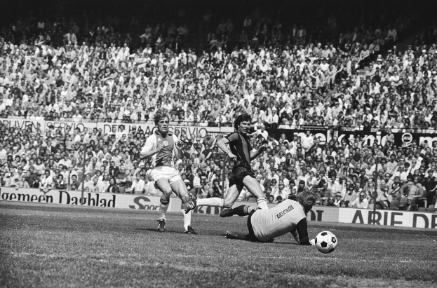 Schwarzes Foto von Männer, die auf einem Feld Füßball spielen, mit Zuschauern im Hintergrund und einem Banner 'Bundesliga 1978-79 Ajax 1-1 Hannover 96'.