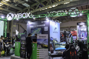Eine Gruppe von Menschen an einem Messestand mit 'Forza Motorsport 5 China', Tischen, Monitoren, Bannern und einem Metalldach im Hintergrund.