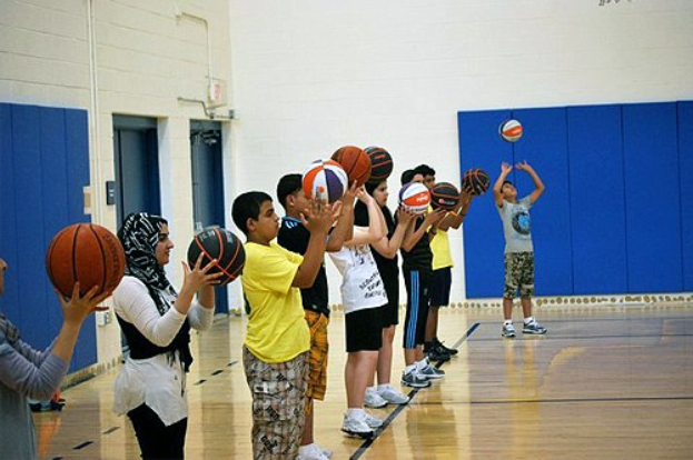 Gruppe von Jugendlichen auf einem Basketballfeld mit Basketballs, mit Türen und einer Wand im Hintergrund.