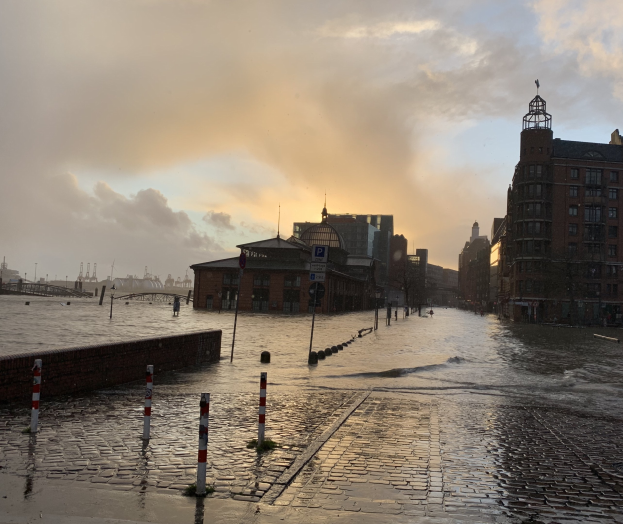Überschwemmte Straße in Hamburg, Deutschland mit Wasser, das Straße, Pfosten, Schilder, Gebäude und eine Brücke bedeckt.