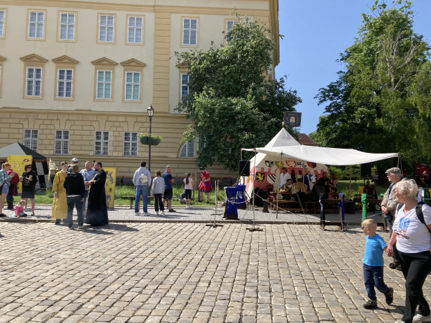 Eine Gruppe von Menschen geht eine Kopfsteinpflasterstraße in Krakau, Polen, entlang, mit Zelten, Tischen und Bäumen an den Seiten, vor einem Gebäude mit sichtbarem Text.