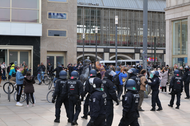 Polizeibeamte mit Helmen stehen vor einer Menge, die Fahrräder hält, mit Glasgebäuden und Fahrzeugen im Hintergrund.