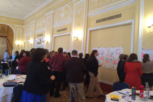 Eine Gruppe von Menschen untersucht Plakate und Charts, die an einer Wand in einem scheinbar künstlerischen Museum angezeigt werden.