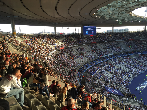 Große Menschenmenge in einem Stadion bei einem Fussballspiel mit einer Bühne, Fahnen und einem Hintergrundbild, das als Allianz Arena in München, Deutschland identifiziert ist.