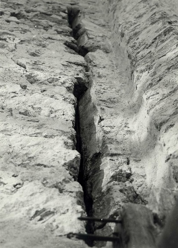 Schwarzes und weißes Foto eines großen Risses im Boden, wahrscheinlich ein Entwässerungskanal, mit einem sichtbaren Wasserzeichen auf der linken Seite.