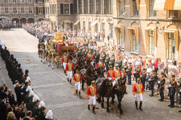 Eine Gruppe von Menschen, die auf Pferden eine Straße entlangreiten, neben einer Menge mit Kameras und Mobiltelefonen, mit Gebäuden und Laternen im Hintergrund während der königlichen Hochzeit von König Willem-Alexander und Königin Maxima der Niederlande.