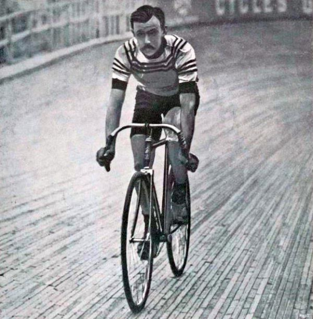 Schwarz-weiß-Foto eines Mannes, der auf einer Bahntrasse Fahrrad fährt, mit einem Zaun und einer Tafel im Hintergrund.