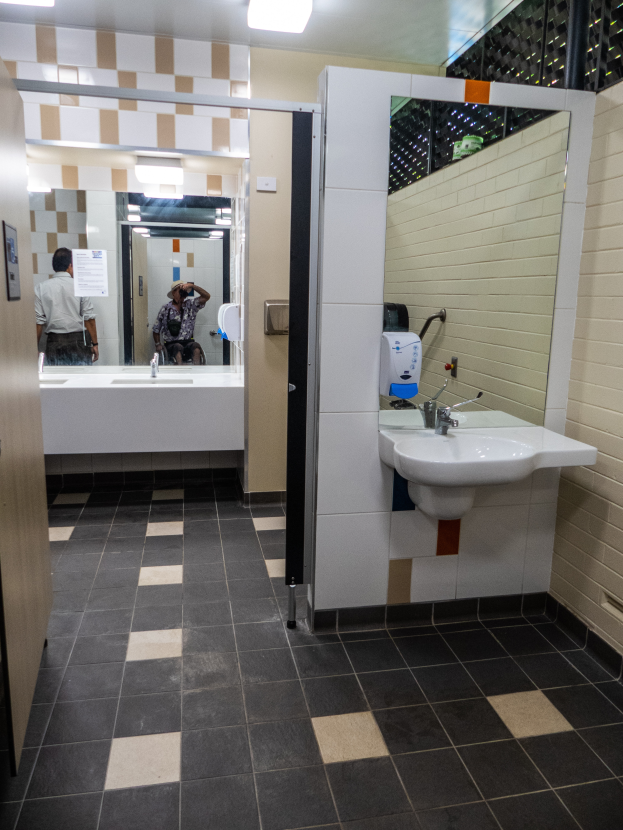 Ein Badezimmer mit Waschbecken, Spiegel und Deckenleuchten, mit einer Person im Spiegel, die eine Kamera hält.