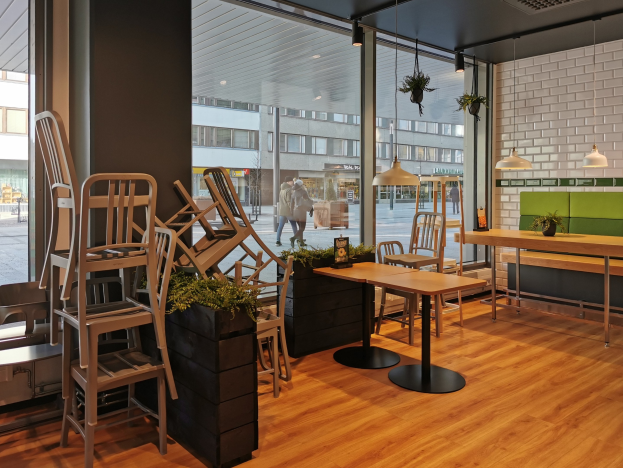 Ein Berliner Restaurant mit Holztischen und -stühlen in der Nähe eines großen Fensters, das eine Außenansicht von Fußgängern, Gebäuden und städtischen Elementen zeigt.