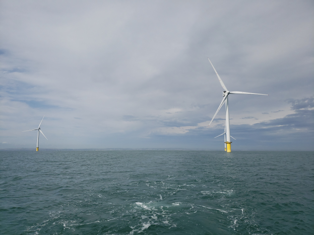 Drei Windräder stehen im Meer, umgeben von Wasser und einem bewölkten Himmel.