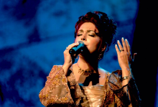 Frau in goldnem Kleid, das in ein Mikrofon singt, auf einer Bühne beim Eurovision Song Contest mit einem blauen und schwarzen Hintergrund.