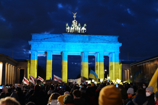 Eine Menschenmenge mit Fahnen und Plakaten steht vor dem Brandenburger Tor in Berlin, Deutschland, mit einer Fahne auf der rechten Seite des Bildes.
