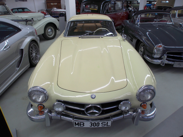 Eine Autohälle mit mehreren Autos, darunter ein Mercedes-Benz 300 SL Roadster, mit Säulen, einem Schrank, einer Wand und Deckenleuchten.