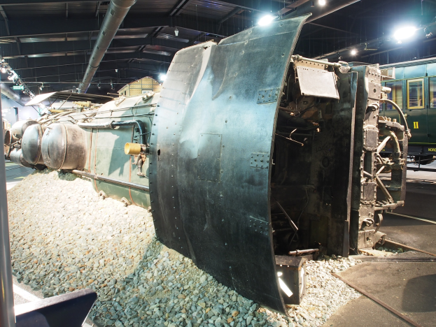 Eine alte Dampflokomotive wird in einem Museum ausgestellt, umgeben von Steinmauern und beleuchtet von Deckenbeleuchtung.