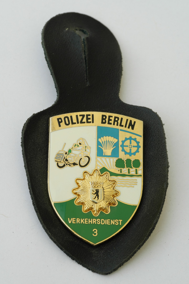 Ein schildförmiges Polizeibadgebnis mit "Polizei Berlin" in schwarzer fetter Schrift, das ein weißes Stern auf einem blauen Hintergrund und einen weißen Rand hat, auf einer Oberfläche platziert.