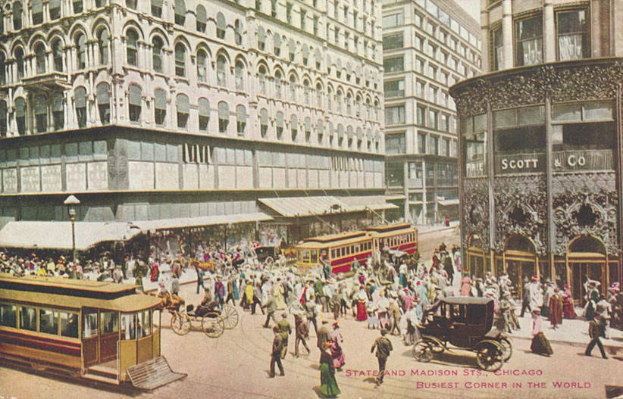 Altes Schwarz-Weiß-Foto einer belebten Stadtstraße mit Fußgängern, Pferdefuhrwerken und Gebäuden mit Fenstern, mit Text am unteren Rand.