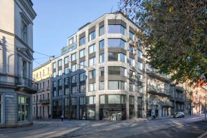 Großes Bürogebäude mit zahlreichen Fenstern, umgeben von Straßeninfrastruktur, Fahrzeugen, Passanten, Bäumen und einem bewölkten Himmel als neue Firmenzentrale.