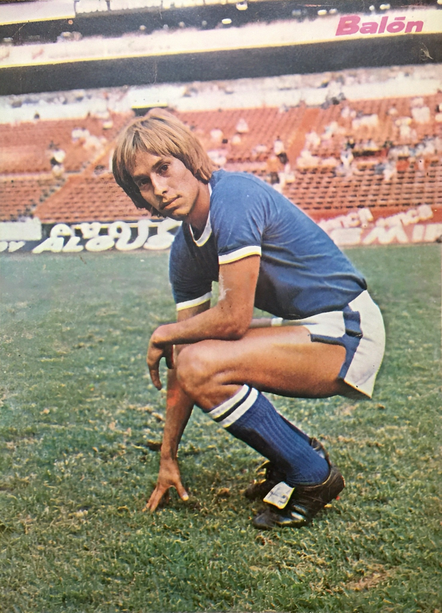 Ein Mann kniet auf einem Fußballfeld, umgeben von Menschen auf Stühlen und Schildern mit Text.