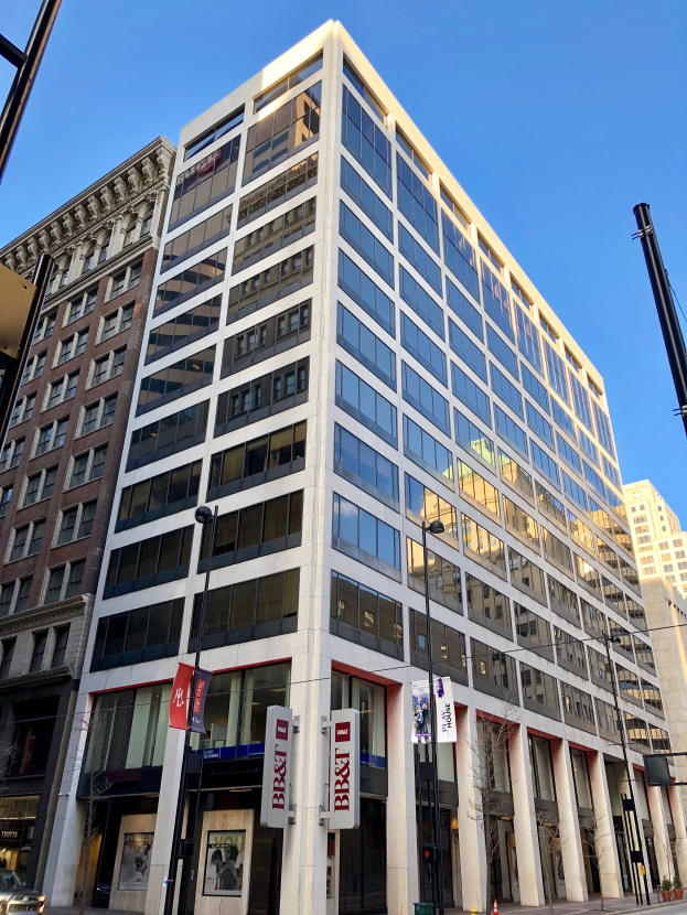 Ein hohes Bürogebäude in Chicago mit vielen Fenstern, umgeben von anderen Gebäuden, Straßenlaternen, Fahrzeugen, Verkehrskegeln, Bäumen und einem bewölkten Himmel.