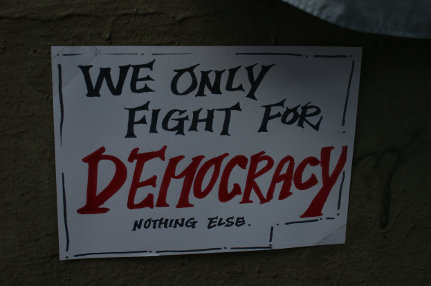Ein weißes Papier mit den Worten "Wir kämpfen nur für Demokratie" darauf, an einer Wand befestigt.