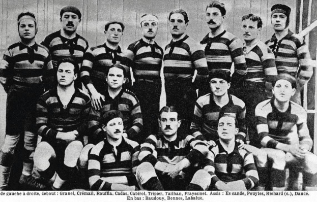 Ein Schwarz-Weiß-Foto einer Rugbymannschaft, einige stehen, einige sitzen, vor einer hölzernen Wand, mit "Lille Rugby Club" unten.