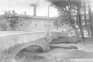 Stadtansicht mit Gebäuden, Bäumen und einer Brücke im Vordergrund, Rauch aus einem Schornstein, unter einem Himmel mit Wasser am Boden.