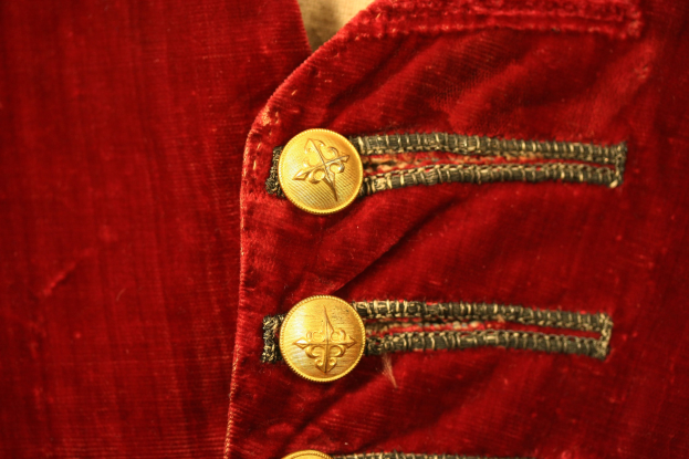 Nahaufnahme einer roten Samtjacke mit goldenen Knöpfen, die einen luxuriösen und eleganten Look vermittelt.