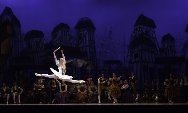 Eine Ballerina in einem weißen Tutu und Spitzenschuhen tanzt auf der Bühne, während das Publikum zusieht, mit einem Schlossgemälde im Hintergrund.