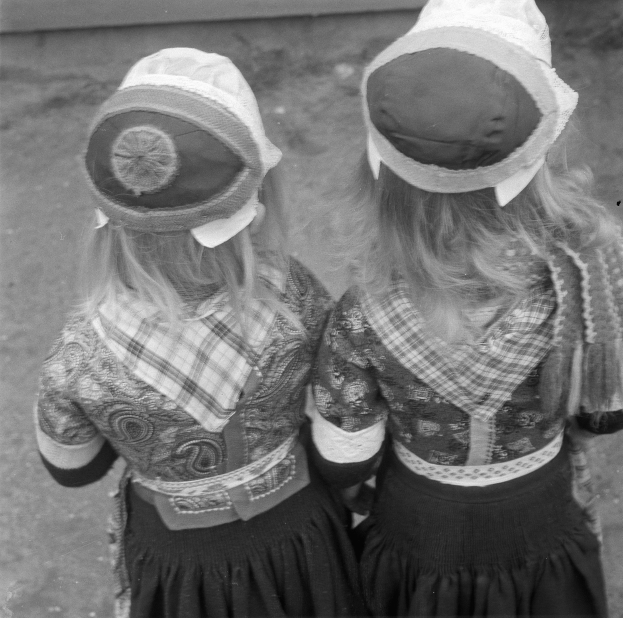 Zwei junge Mädchen in traditionellen bayrischen Kleidern und Hüten stehen Seite an Seite gegen eine Wand in einem Schwarz-Weiß-Foto.