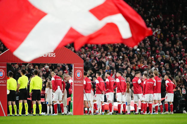Eine Gruppe von Menschen auf einem Fussballfeld mit einer roten und weissen Flagge im Vordergrund, ein Torbogen mit dem Text "Bayern Munich vs Bayern Munich Betting Tips & Preview" im Hintergrund und eine grosse Menge im Stadion.