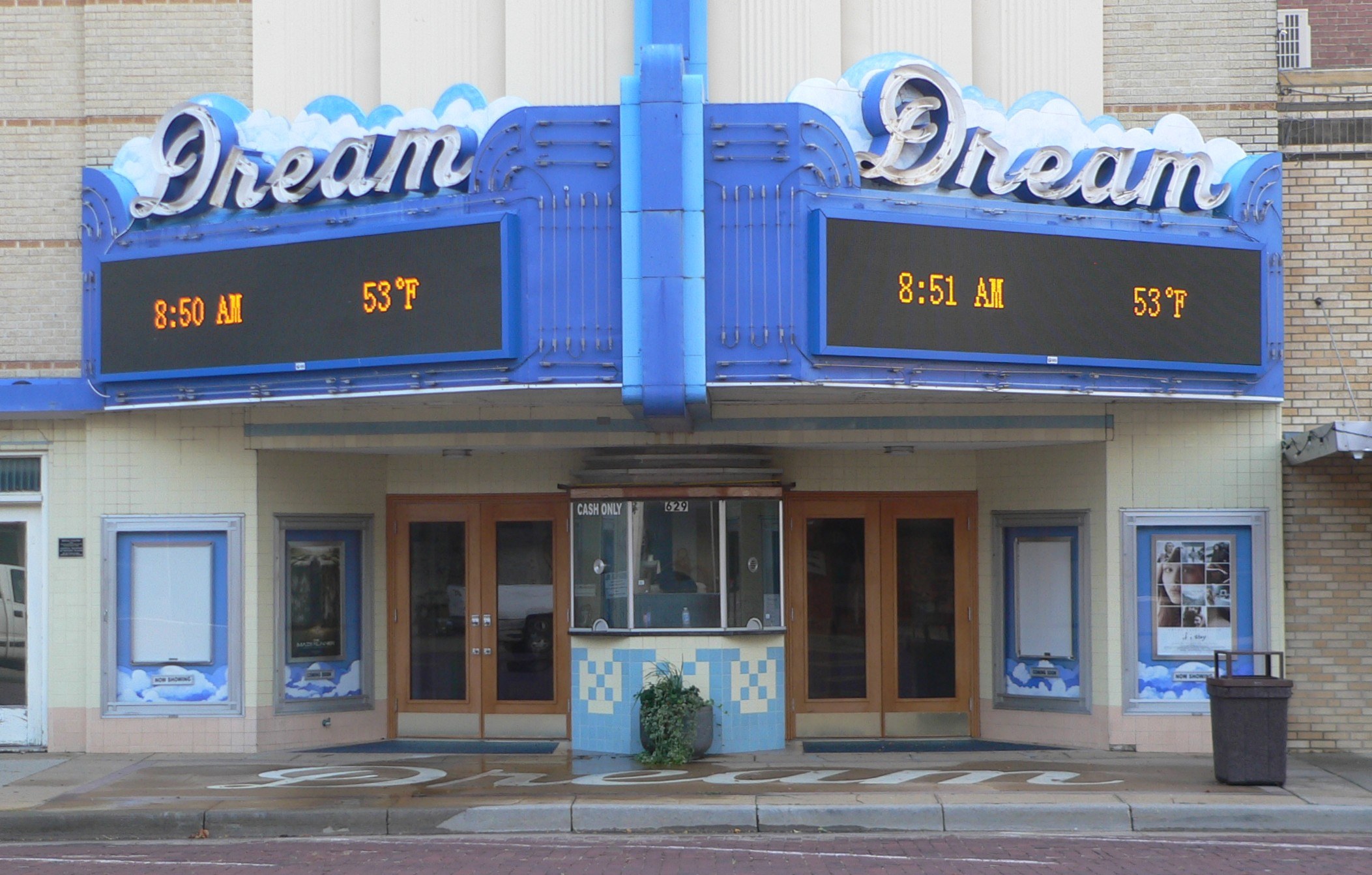 Außenansicht des Dream Theaters in St. Louis, Missouri, mit Glastüren und -fenstern, einem Namen Schild, einem Müllbehälter, einem Topfpflanze und einer Straße unten.