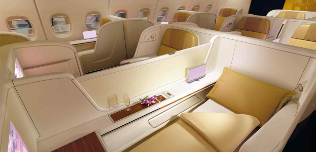 Das Innere einer Singapore Airlines A380 Business Class Kabine mit bequemen Sitzen, einem Tisch mit einer Blumenvase, Gläsern und anderen Gegenständen sowie Fenstern auf beiden Seiten.