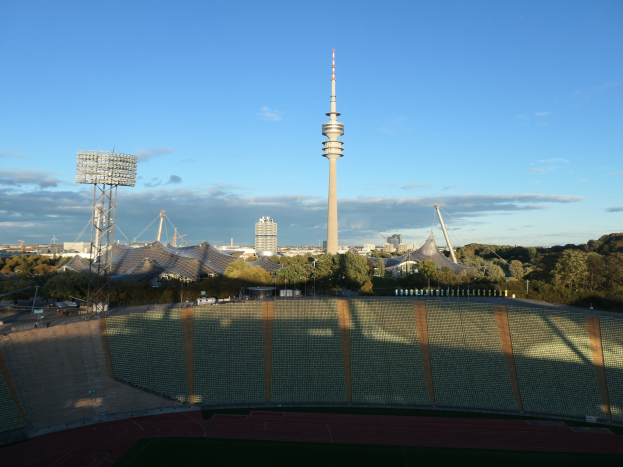 Olympiastadion in Berlin, Deutschland, mit dem Fernsehturm im Hintergrund, umgeben von B"umen, Geb"uden und Lichtern unter einem bew"olkten Himmel.