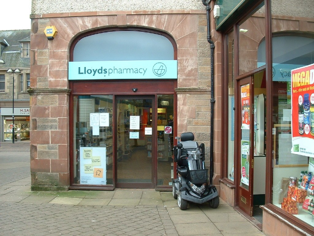 Eine Apotheke mit einem vor dem Gebäude geparkten Auto und einem Gebäude auf der linken Seite.