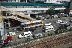 Eine belebte Stadtstraße mit Fahrzeugen, Gebäuden, Grünflächen und verschiedenen städtischen Elementen einschließlich Schildern und Bahnschienen.