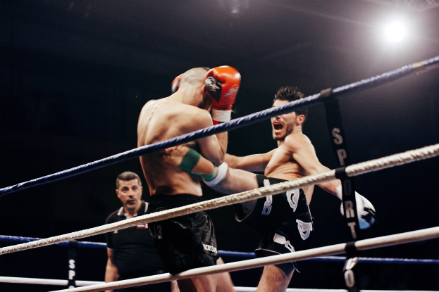 Zwei Boxer im Ring, die sich gegenseitig mit Faustschlägen attackieren, während ein Schiedsrichter im Hintergrund zusieht.