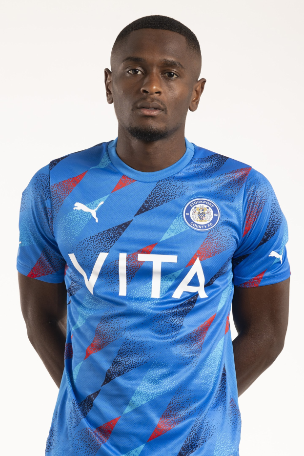 Ein Mann in einem blauen Auswärtsshirt von Leicester City aus der Saison 2018-19 steht mit Händen in den Taschen und einem leichten Lächeln, trägt ein leichter, atmungsaktiver Rundhals-Shirt mit kurzen Ärmeln und dem Team-Logo auf der Vorderseite.