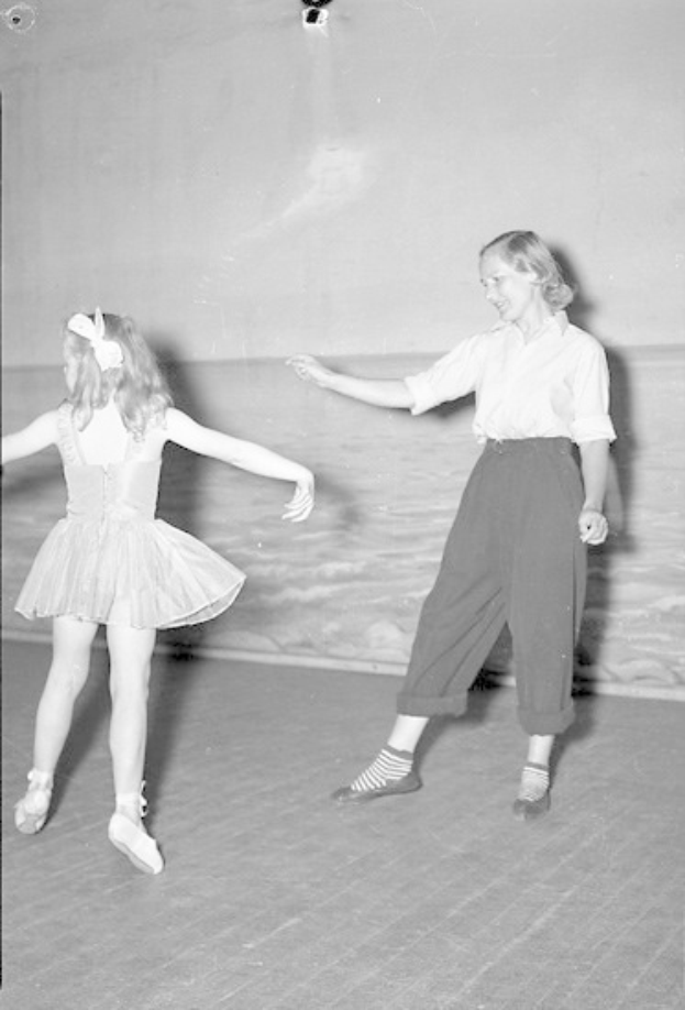 Zwei junge Mädchen in Schuhen tanzen auf einer Bühne mit einer Wand im Hintergrund.