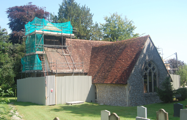 Kirche mit einer grünen Plane auf dem Dach, umgeben von einem Metallzaun, Bäumen, Pflanzen, Gras, einem Pfad, Polen und einem bewölkten Himmel.