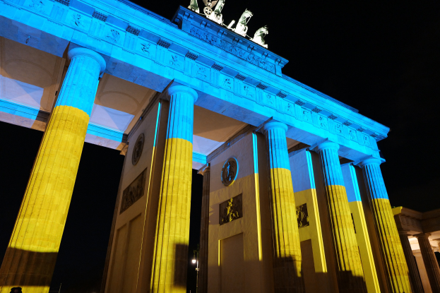 Erleuchtetes Brandenburger Tor in Berlin, Deutschland, mit blauen und gelben Lichtern, mit Skulpturen vor dunklem Hintergrund.