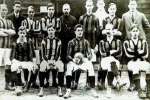 Ein Schwarz-Weiß-Foto einer Fußballmannschaft, einige stehen, einige sitzen, vor einer Wand, mit dem Text "Ballymena Football Club" unten.